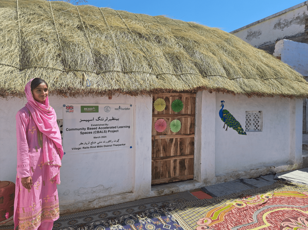 A girl wearing pink clothing stood next to a white building that has a peacock draw on it